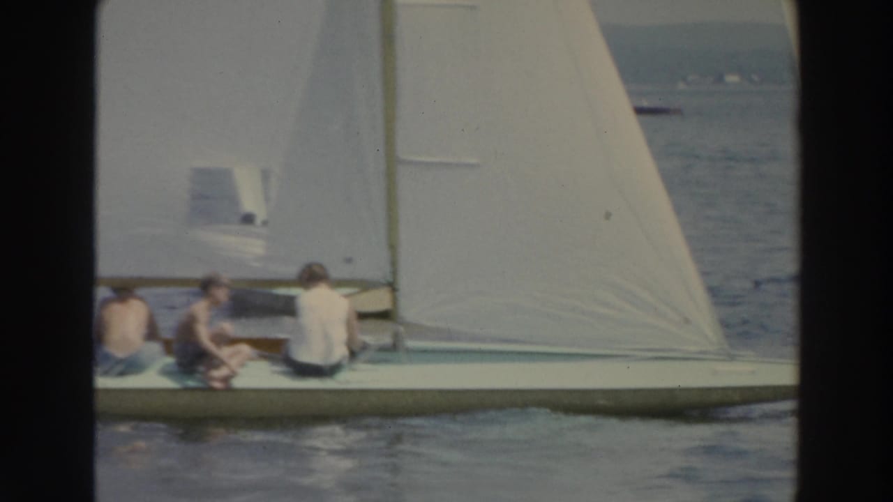 White sailboat with seated people moving across a lake.