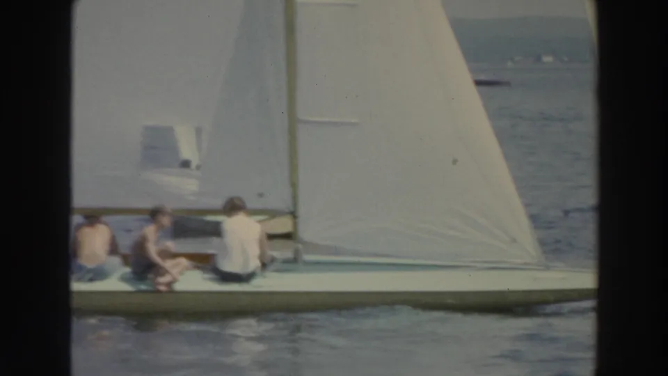 1966 Wisconsin 8mm frame showing a white sailboat with seated people crossing open lake water near a distant shore.