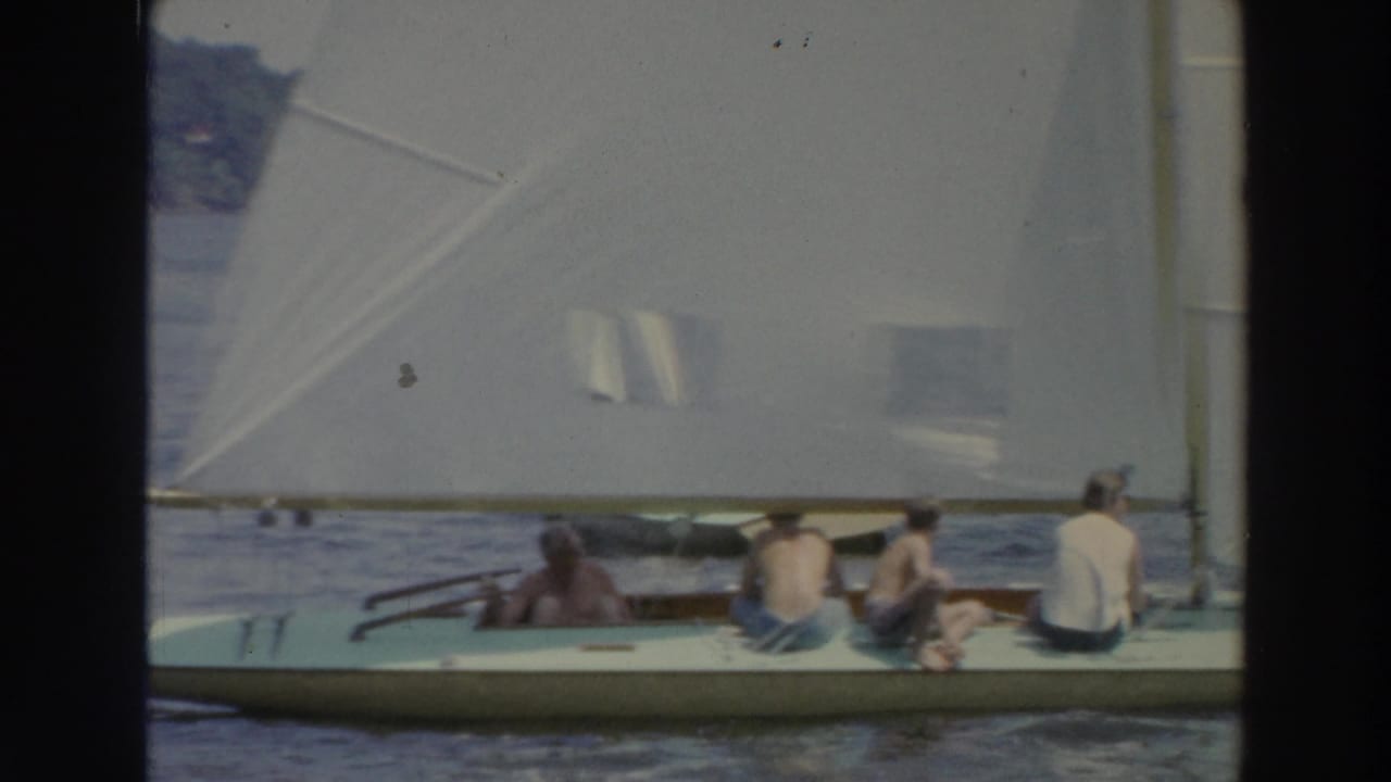 People seated in a white sailboat beside a large sail.