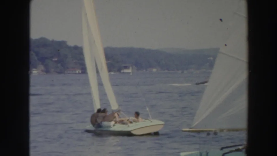 1966 Wisconsin 8mm frame showing a small sailboat with people aboard near another white sail on open water.