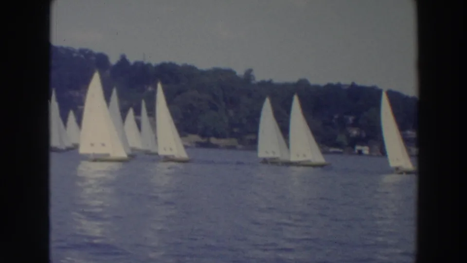 1966 Wisconsin 8mm frame showing a larger group of sailboats racing or gathering on a lake near a wooded shore.
