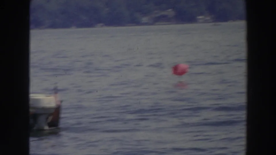 1966 Wisconsin 8mm frame with a red buoy on the lake and the edge of a small motorboat in the foreground.