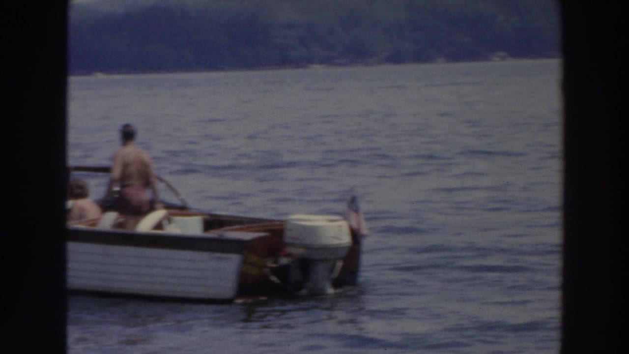 1966 Wisconsin 8mm frame showing a white motorboat with people aboard on blue lake water, with a wooded shore in the distance.