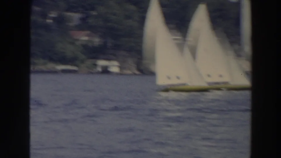 1966 Wisconsin home-movie frame with several white-sailed boats clustered on blue lake water beside a distant wooded shore.