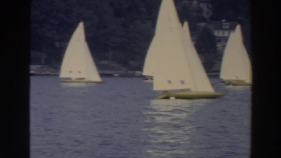 1966 Wisconsin 8mm frame showing three small sailboats on rippled water, with hillside houses and trees in the background.