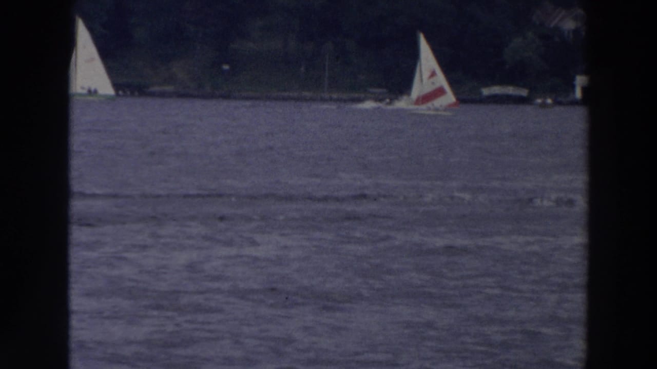 1966 Wisconsin 8mm frame showing sailboats on open lake water with trees and distant shoreline structures in the background.