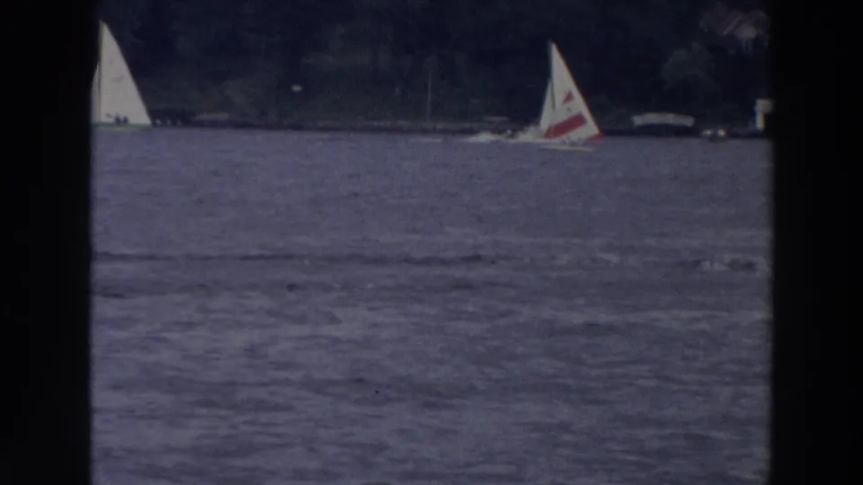 1966 Wisconsin 8mm frame showing sailboats on open lake water with trees and distant shoreline structures in the background.