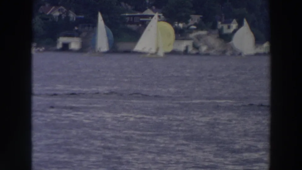 1966 Wisconsin 8mm frame showing sailboats spread across a lake, with soft focus, shoreline homes, and trees behind them.