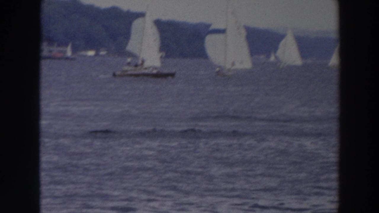 1966 Wisconsin 8mm frame showing sailboats racing across a bay with white sails and spinnakers against a tree-lined shore.