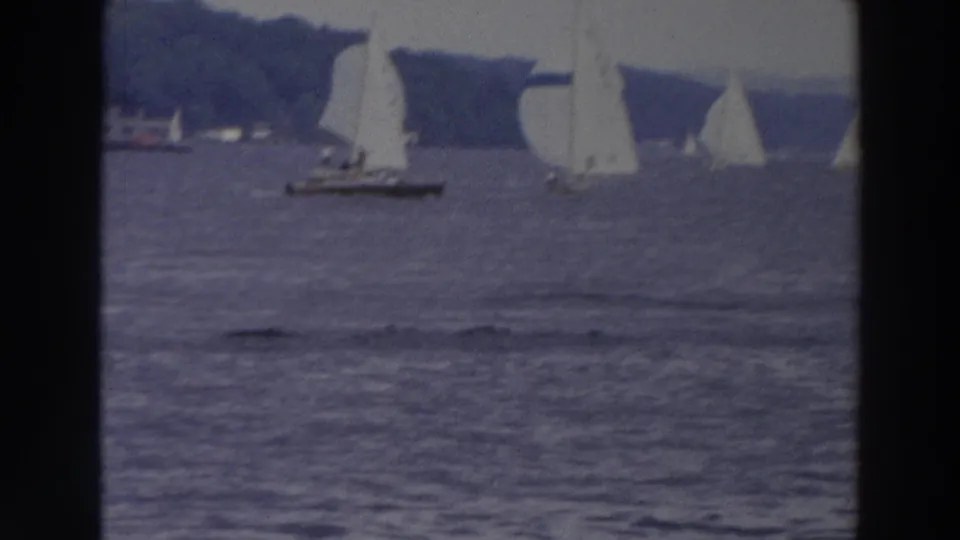 1966 Wisconsin 8mm frame showing sailboats racing across a bay with white sails and spinnakers against a tree-lined shore.