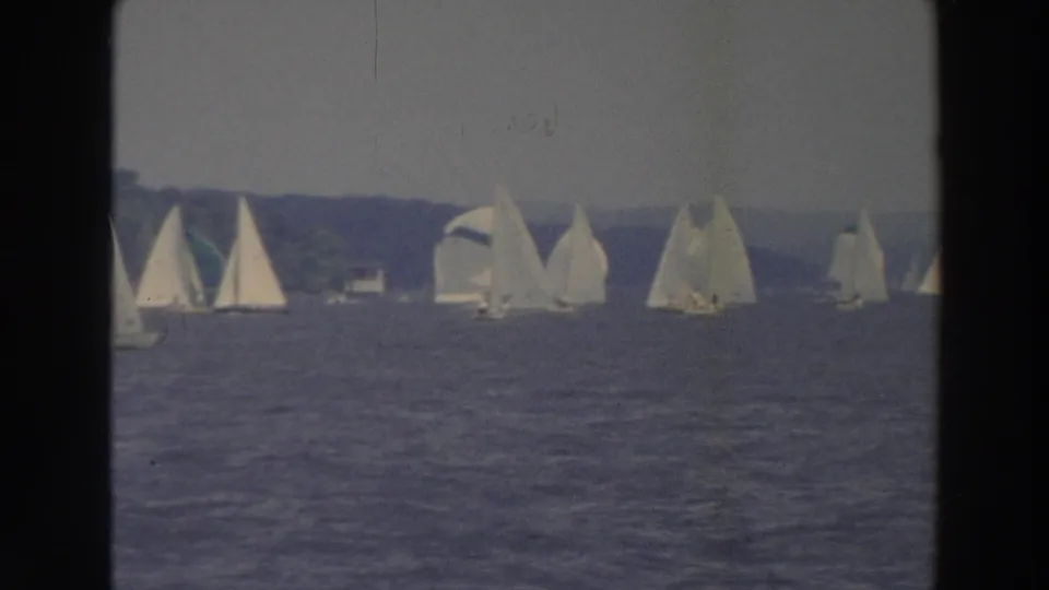 1966 Wisconsin home-movie frame showing several sailboats moving across blue lake water near a low wooded horizon.