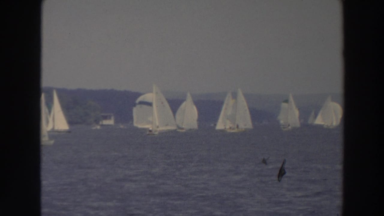 1966 Wisconsin 8mm frame showing multiple sailboats spread across a lake under a hazy sky.