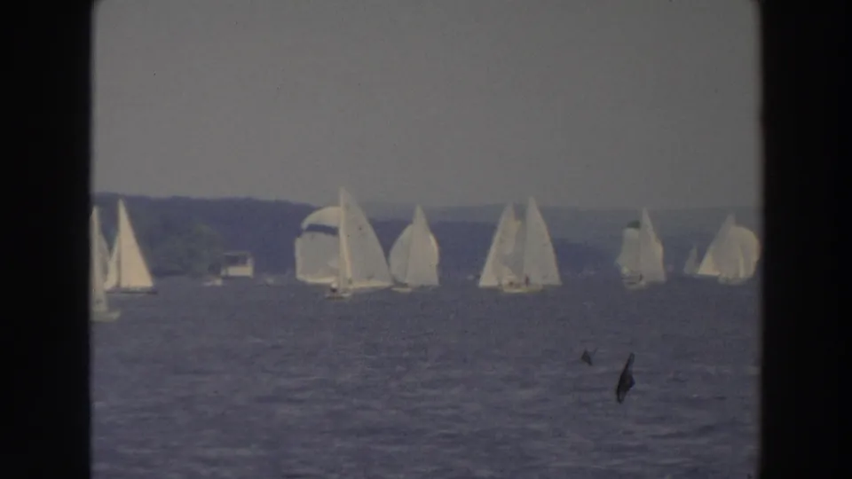 1966 Wisconsin 8mm frame showing multiple sailboats spread across a lake under a hazy sky.