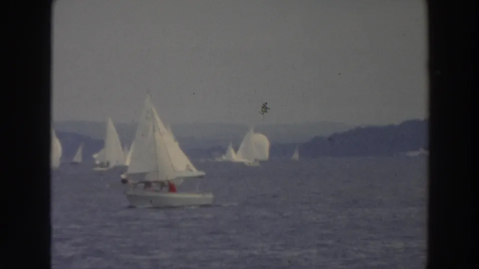 1966 Wisconsin home-movie frame with a small motorboat near racing sailboats on a lake.
