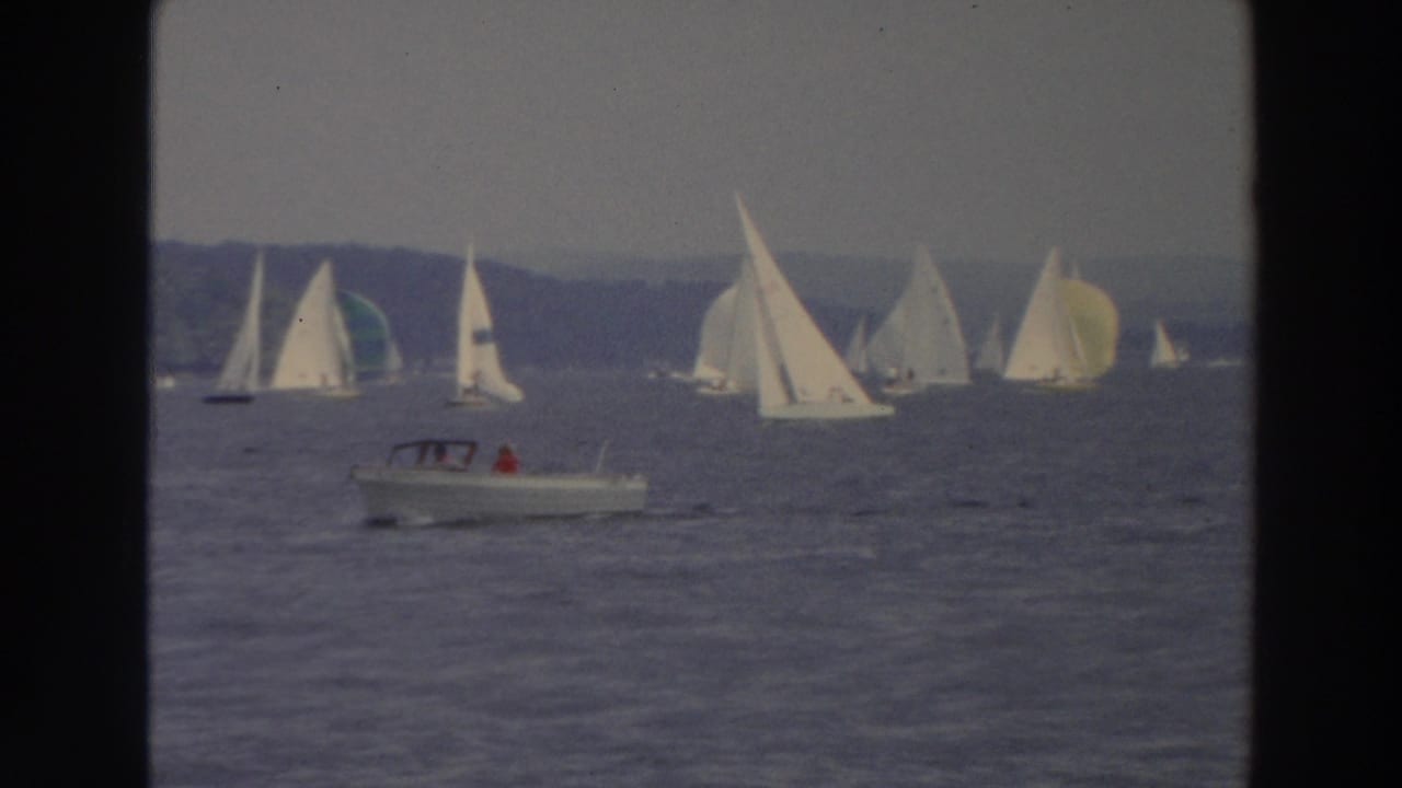 1966 Wisconsin 8mm frame with a small motorboat in front of a lake fleet of white sailboats.