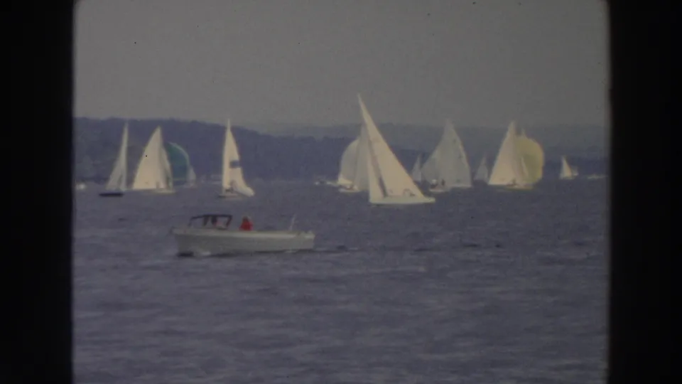 1966 Wisconsin 8mm frame with a small motorboat in front of a lake fleet of white sailboats.