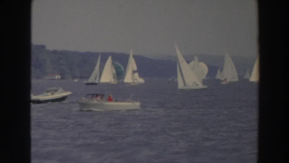 1966 Wisconsin 8mm frame showing a motorboat below clustered sailboats near a wooded lakeshore.