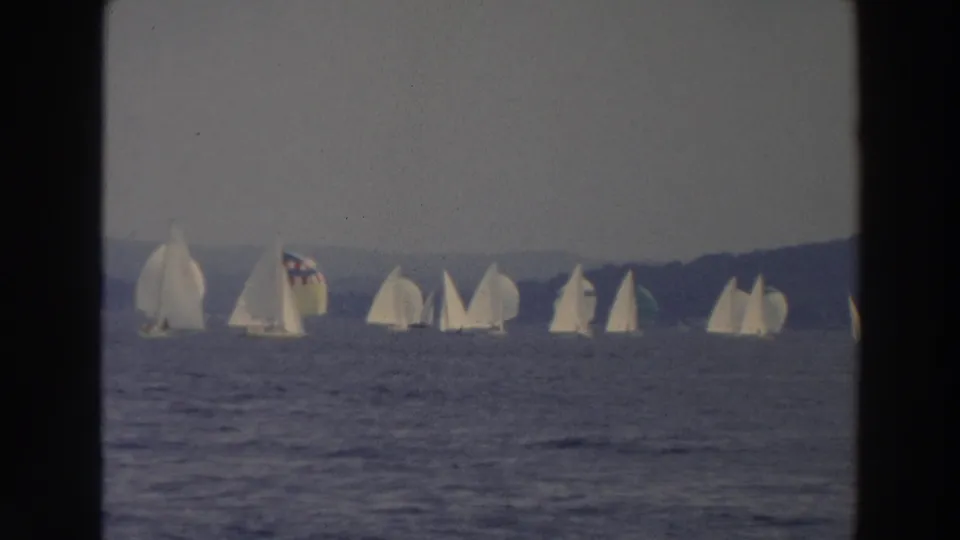 1966 Wisconsin 8mm frame showing a small fleet of white sailboats on rippled lake water near a distant wooded shore.