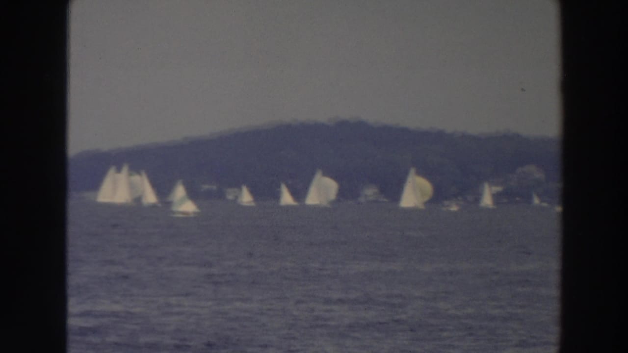 1966 Wisconsin home-movie frame showing multiple white sailboats on open lake water with a tree-lined shore in the distance.