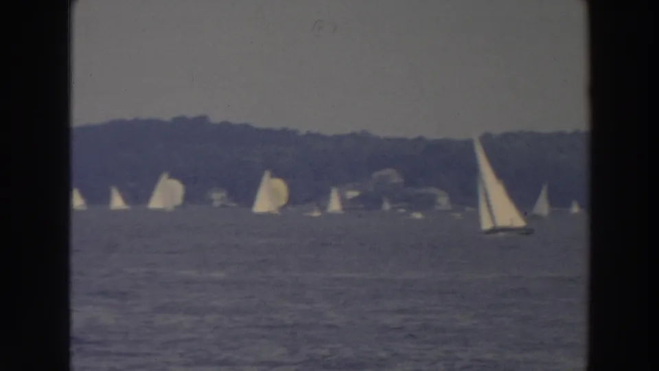 Wide 1966 Wisconsin lake view with scattered sailboats and a larger sailboat passing near the right side of frame.