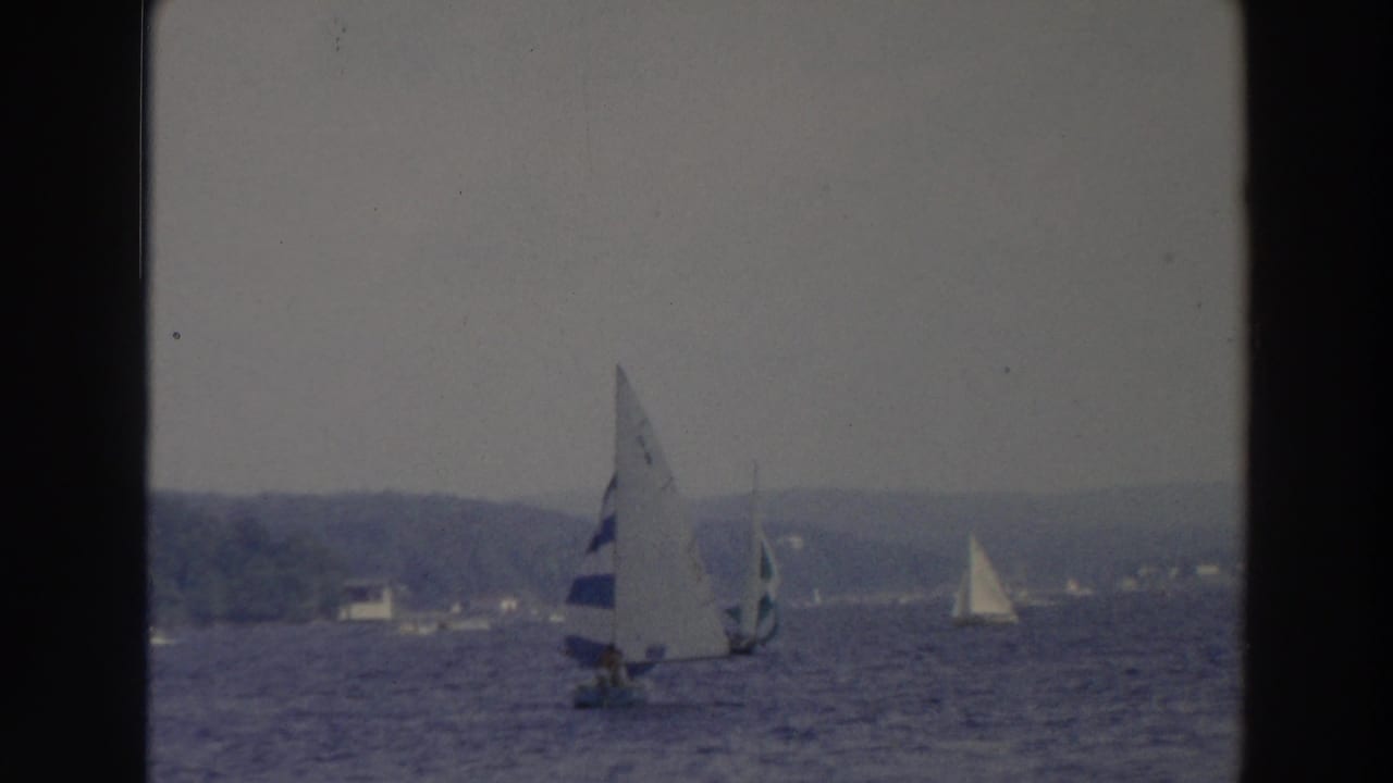 1966 Wisconsin 8mm frame showing several small sailboats on a lake under a hazy overcast sky.