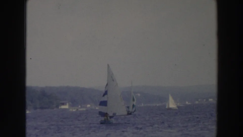 1966 Wisconsin 8mm frame showing several small sailboats on a lake under a hazy overcast sky.