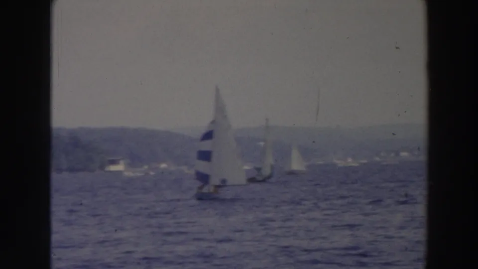 Vintage 8mm frame from Wisconsin showing a blue-striped sailboat with other small sailboats beyond it.