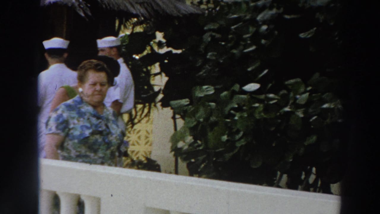 1966 Wisconsin vacation footage frame with a woman by a white railing and Navy personnel partly visible behind plants.