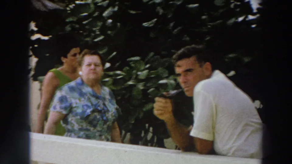 1966 Wisconsin home-movie frame showing vacation visitors behind a white railing, including a man in a white shirt facing the lens.