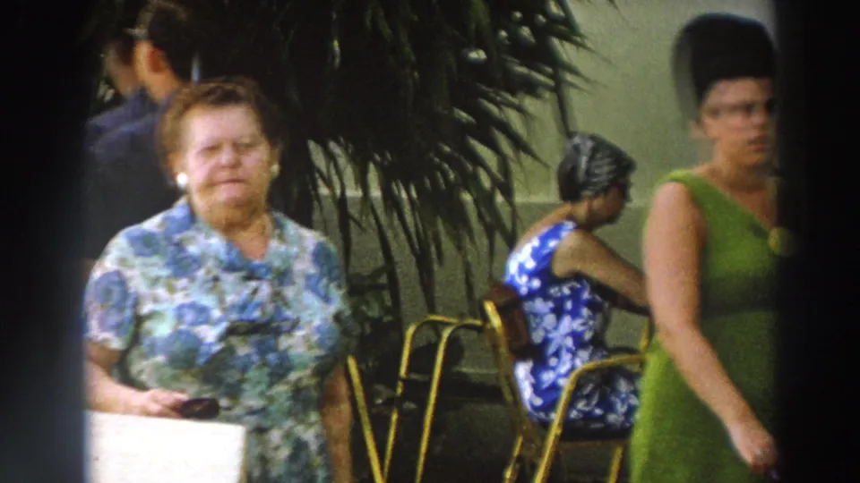 1966 Wisconsin home-movie still showing women walking by outdoor chairs and seated guests at a crowded venue.