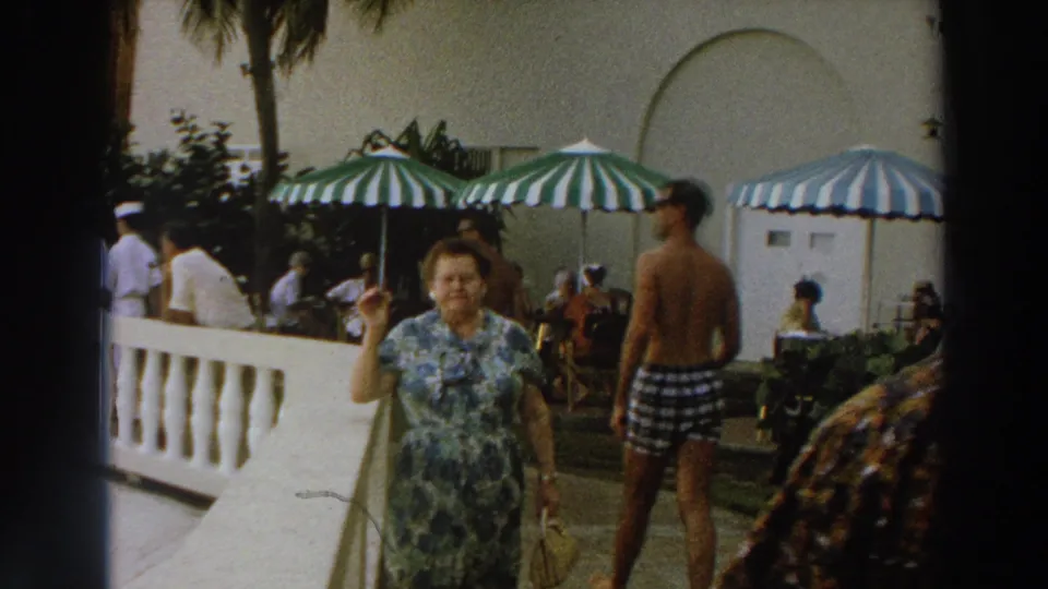 1966 Wisconsin patio scene with a woman in a floral dress raising her hand as resort guests move behind her.