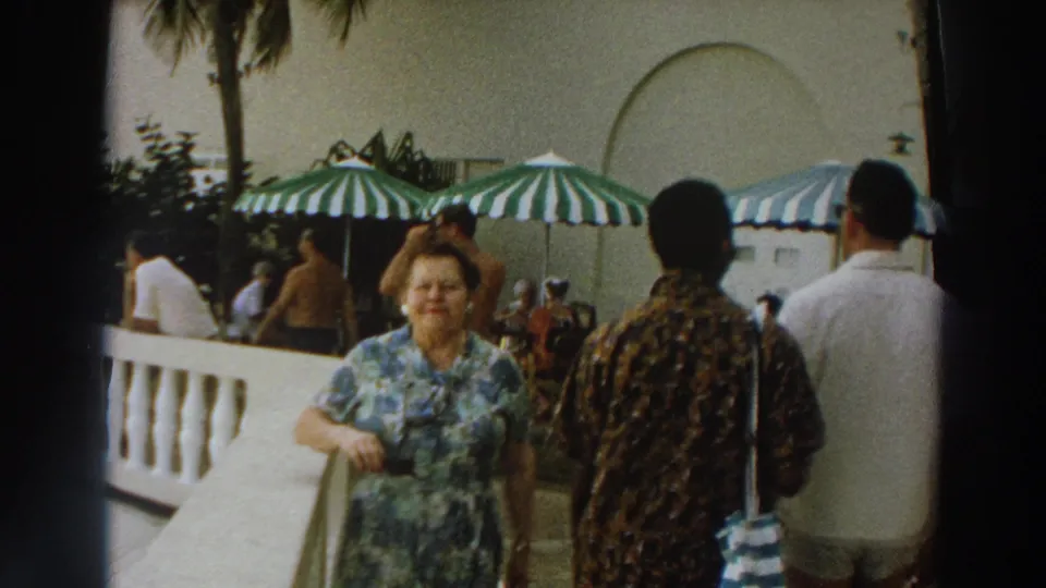 1966 Wisconsin resort patio frame showing a woman near the foreground with men passing in the opposite direction behind her.