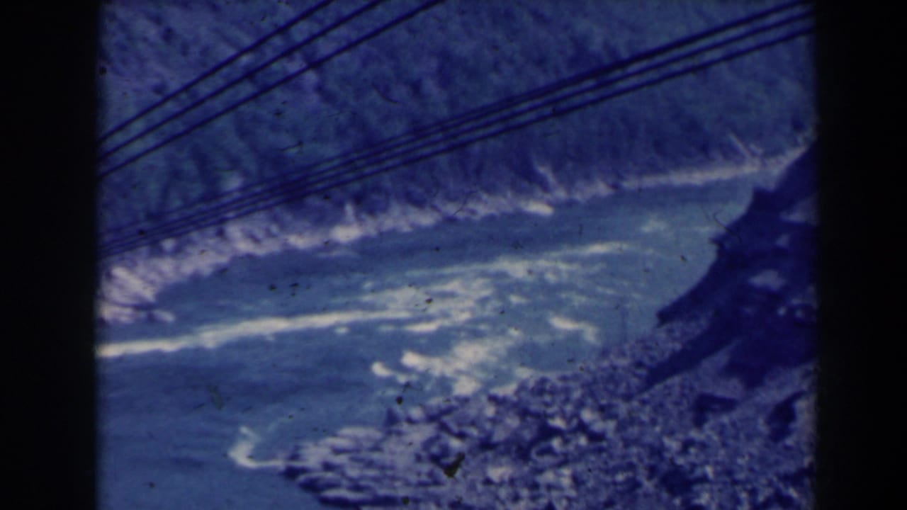 1963 8mm view over Niagara Gorge, with churning blue water, rocky banks, overhead cables, and dark film-frame borders.