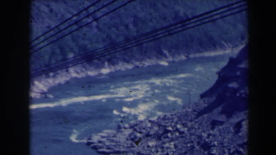 1963 8mm view over Niagara Gorge, with churning blue water, rocky banks, overhead cables, and dark film-frame borders.