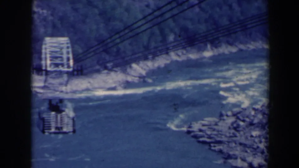 1963 Niagara Gorge cable-car scene, showing the white terminal structure, suspended car, overhead cables, rocky banks, and river below.