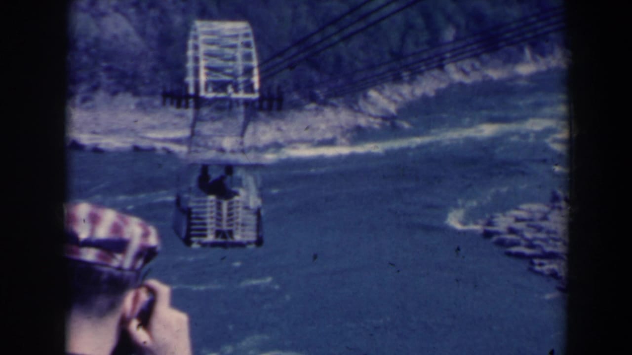 1963 home-movie frame at Niagara Falls, Canada, showing a tourist in a plaid cap filming a cable car over the river.