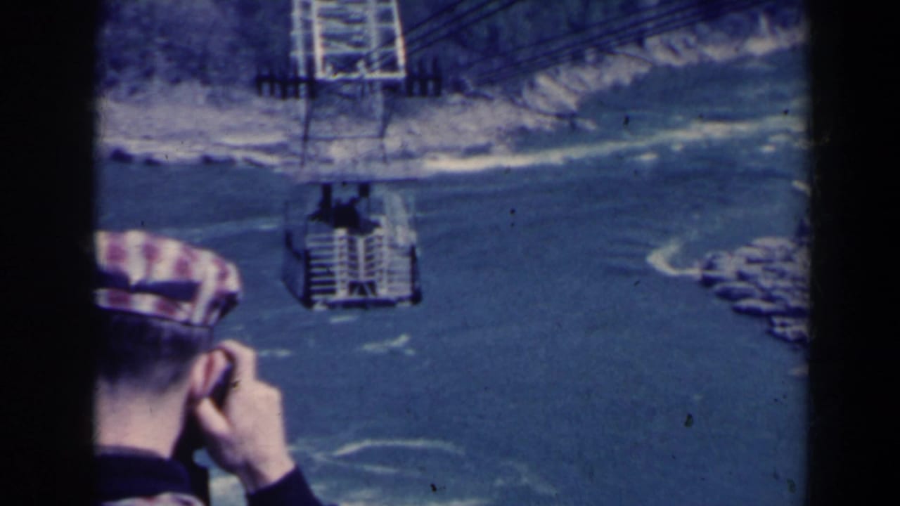 Cable car hangs over the river with a tourist in the foreground.