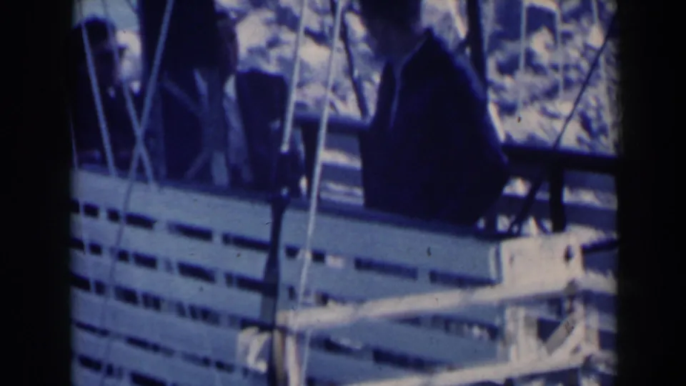 Home-movie view of cable car passengers, including a suited man, seated inside an open cabin at Niagara Falls.