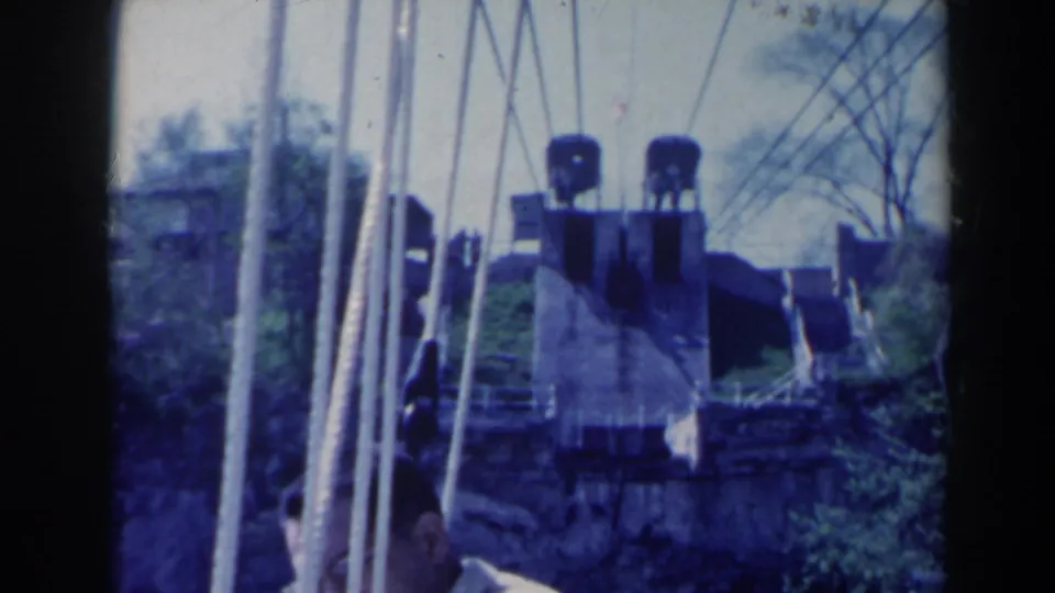 1963 Niagara Falls, Canada frame with a man partly visible at lower left beside poles, railings, and industrial equipment.
