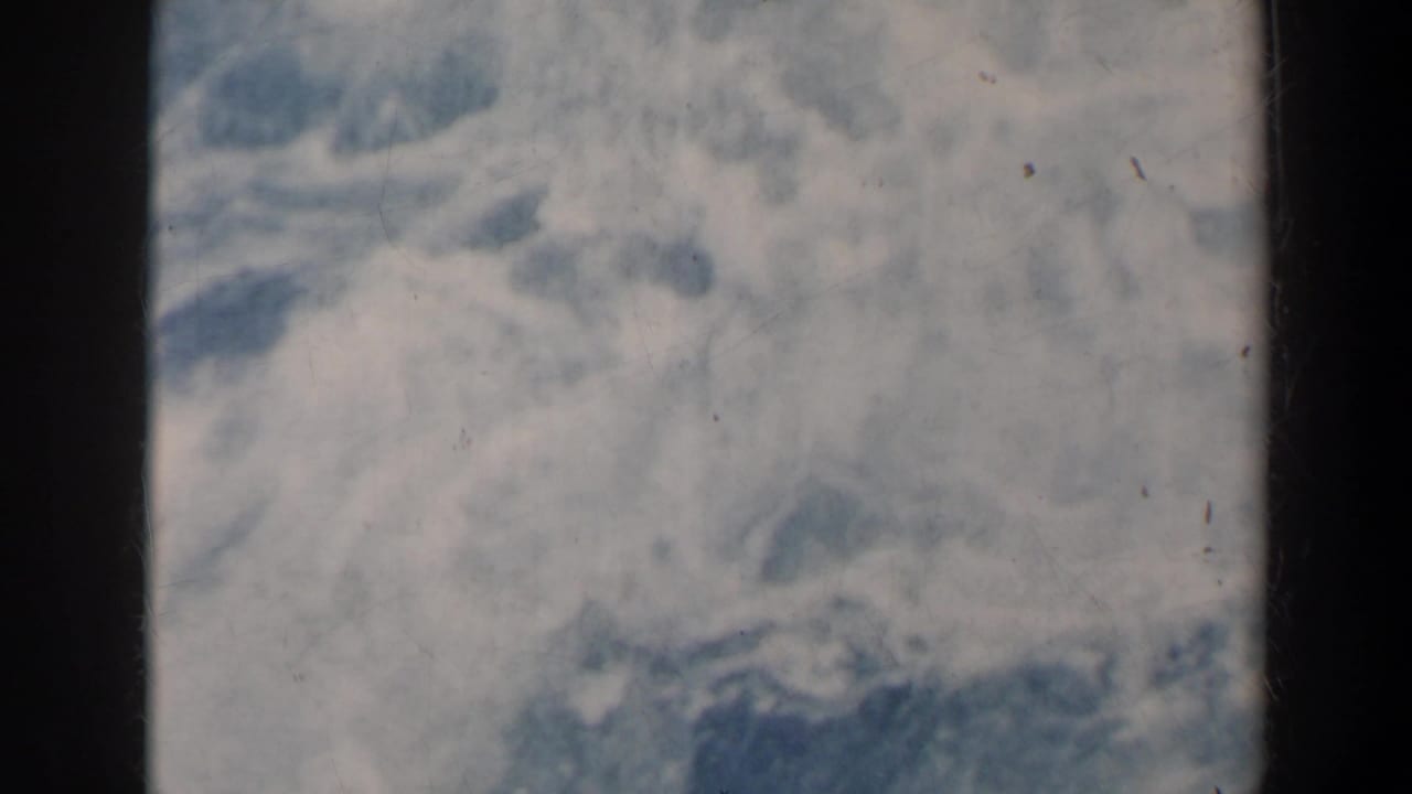 1963 8mm frame with indistinct cloudy sky or haze and dark vertical film-frame edges.