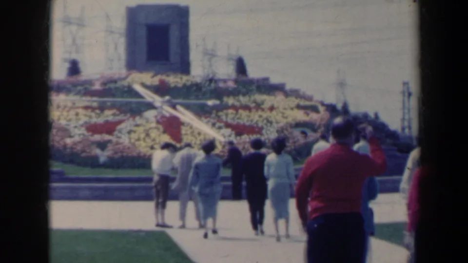 A visitor-shot 1963 Niagara Falls garden scene shows people in suits, dresses, and coats walking past lawns and a large floral display.