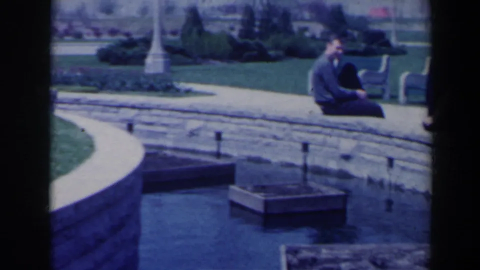 Visitor-shot 1963 garden view near the Niagara Falls Floral Clock, with two people seated by a water channel and formal paths.
