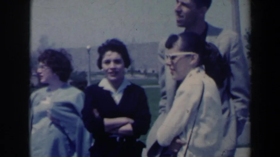 A 1963 Niagara Falls home-movie frame shows young adults gathered outdoors, with sunglasses, glasses, and park grounds visible.