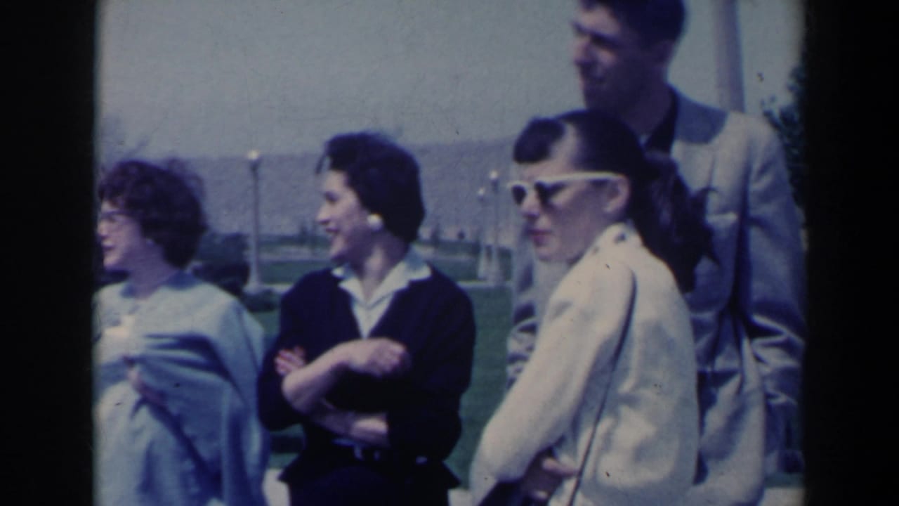1963 Niagara Falls home-movie frame showing young adults in period clothing standing outdoors near a lawn and walkway.