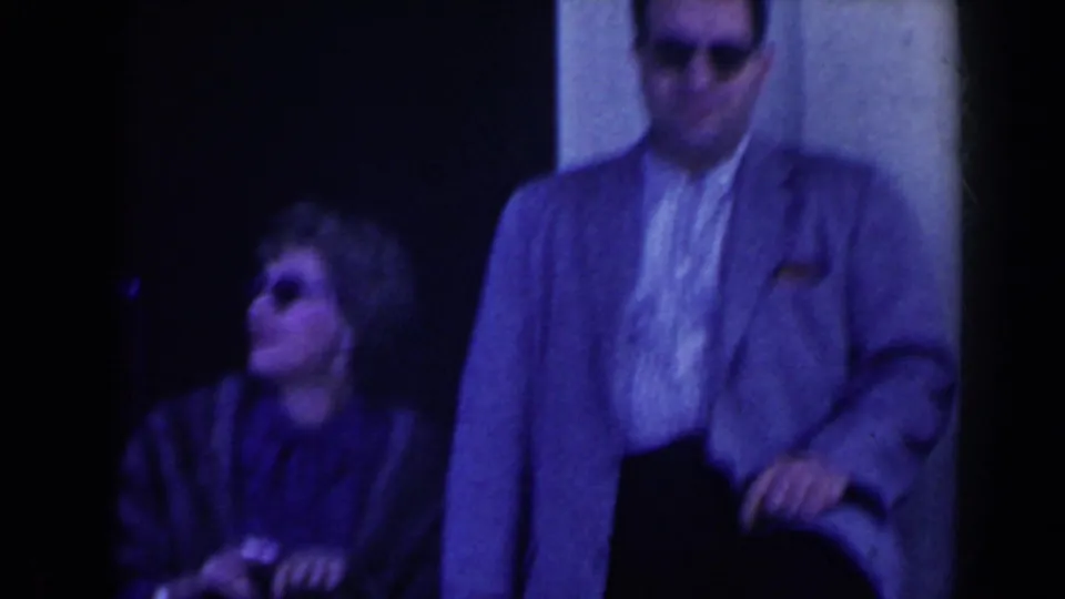 Close 1963 Niagara Falls travel shot with a man in a light jacket and a seated woman in sunglasses near a dark entrance.
