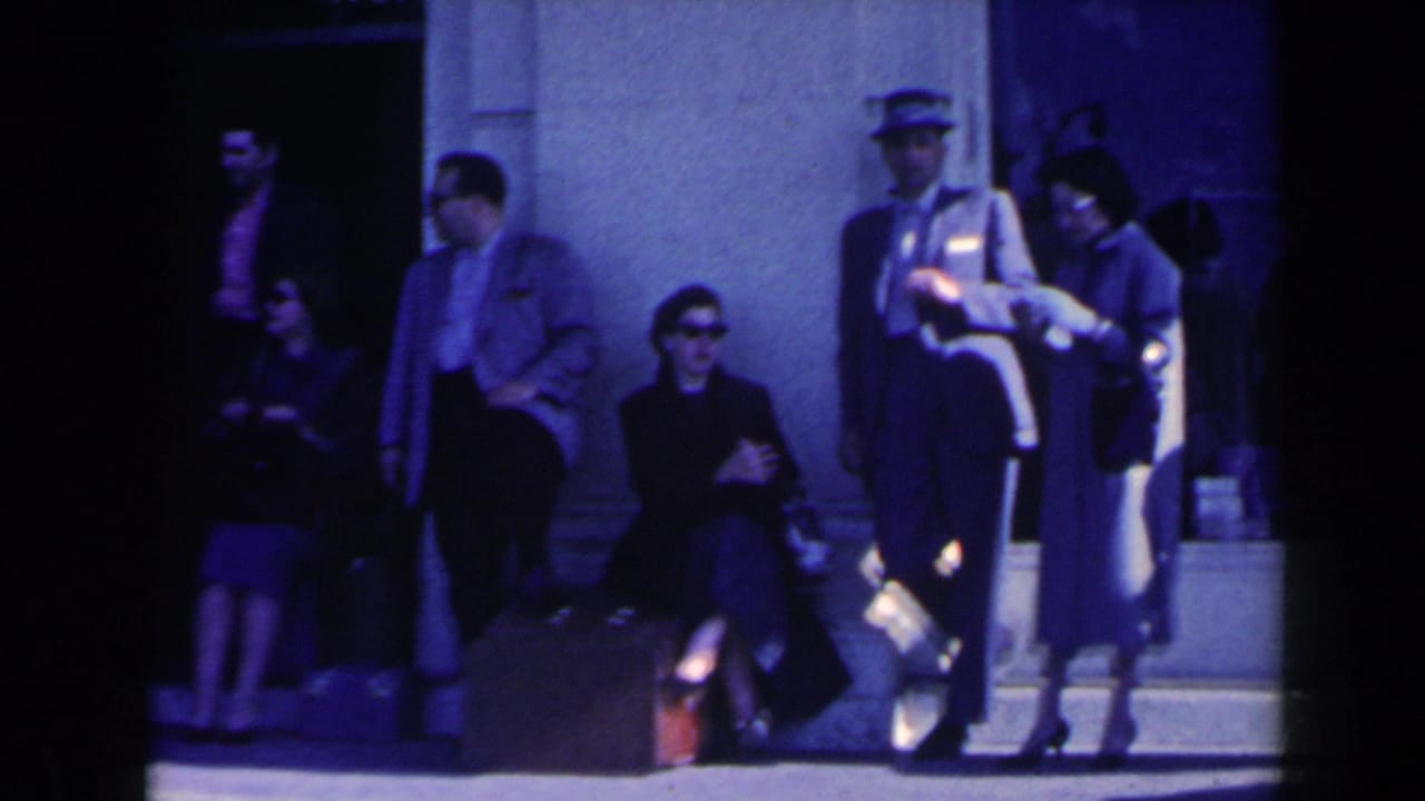 People standing and sitting on steps outside a building, with a uniformed attendant nearby.