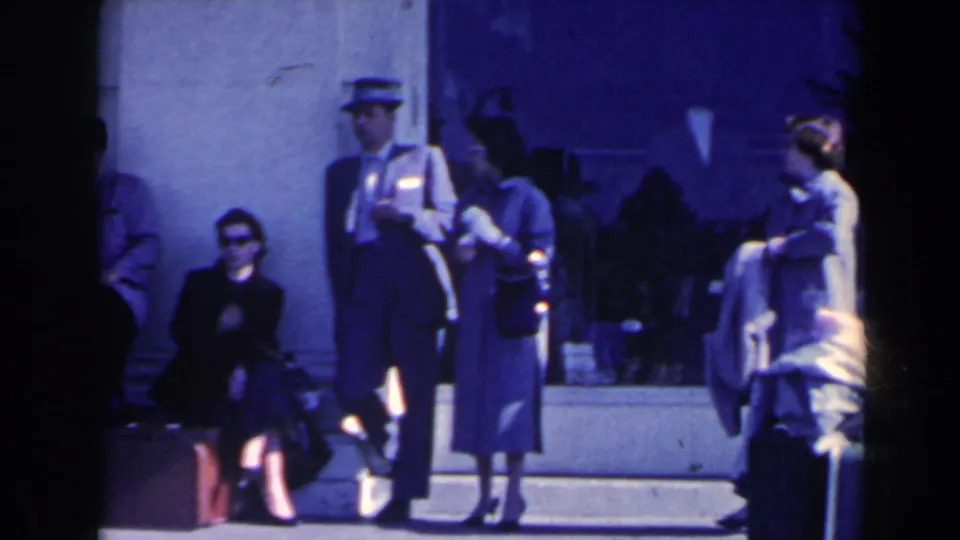 1963 Niagara Falls home-movie frame showing people waiting outside a building with luggage and a uniformed attendant present.