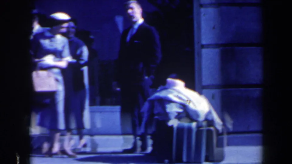 Adults with hats and suitcases stand outside a stone building in a blue-toned 1963 Niagara Falls travel moment.