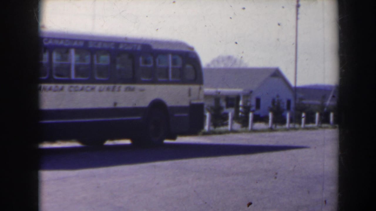 1963 Niagara Falls Canada footage showing the rear side of a Canada Coach Lines bus near pavement, bollards, and a small white building.