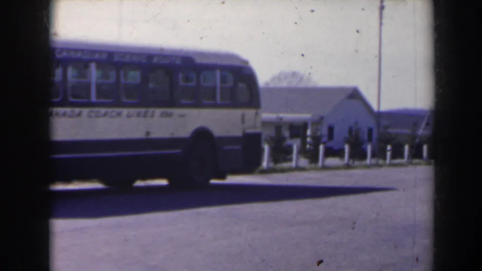 1963 Niagara Falls Canada footage showing the rear side of a Canada Coach Lines bus near pavement, bollards, and a small white building.